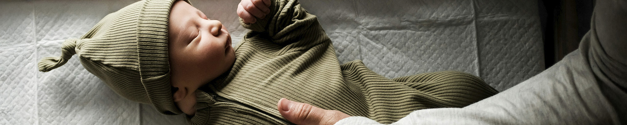 Parent resting hand on newborn baby in hospital bassinet.