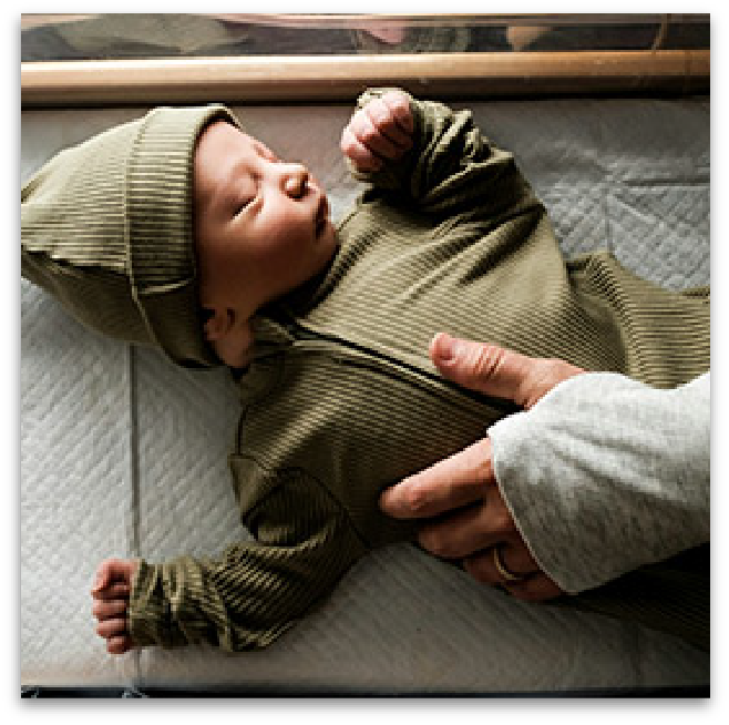 Parent resting hand on newborn baby in hospital bassinet.