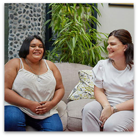 Two smiling women sitting on a couch.
